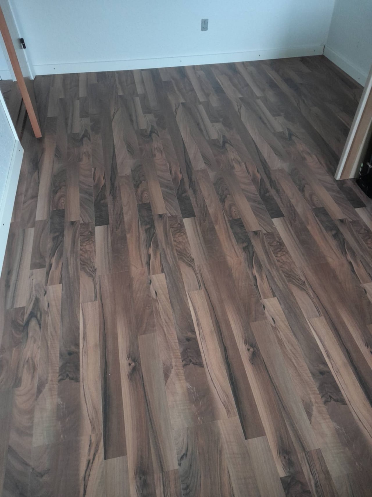 Neu verlegter dunkler Laminatboden im leeren Raum, weiße Sockelleisten und sauberer Zuschnitt am Türrahmen